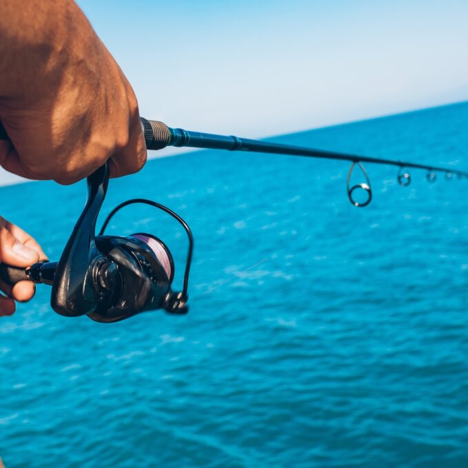 Man holding Fishing rod tackles close up. Hand with spinning reel. Fisherman standing and throw a fishing rod while fishing at the sea background.